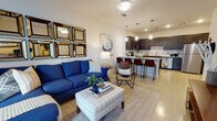 This single-floor residence offers a thoughtfully designed open-concept layout that seamlessly connects the living, dining, and kitchen areas. The living room serves as the heart of the space, featuring a sliding glass door that invites natural light and provides patio access. A decorative grid of framed mirrors accents the main wall, adding depth and visual interest to the room.

The kitchen is both functional and stylish, outfitted with rich dark-stained cabinetry, granite countertops, a classic white subway tile backsplash, and a full suite of stainless steel appliances including a refrigerator, range, microwave, and dishwasher. A kitchen island with bar seating provides an ideal space for casual dining and entertaining.

The bedroom is a serene retreat highlighted by a bold blue accent wall, large windows dressed with patterned curtains and light-filtering blinds, and plush carpeted flooring. The room offers generous space for a full bedroom suite.

The bathroom continues the design language of the home with matching dark cabinetry, granite countertops, a tiled tub-shower combination, and clean white walls. Throughout the residence, light-toned flooring ties each room together, creating a cohesive and modern aesthetic.