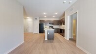 This well-appointed single-story home offers 3 bedrooms and 2 bathrooms across a thoughtfully designed floor plan. The open-concept kitchen and living area serves as the heart of the home, where rich dark-stained cabinetry contrasts beautifully with light granite countertops and a central island that provides additional prep space and seating. Black appliances, including a refrigerator, range, microwave, and dishwasher, complete the kitchen. Light wood-style flooring flows seamlessly throughout the main living areas and bedrooms, creating a cohesive and modern aesthetic. The living room is bright and airy, featuring a ceiling fan and French doors that invite natural light and outdoor access. The generously sized primary bedroom includes its own ceiling fan, a closet, and connects to a well-designed en-suite bathroom boasting a dual-sink granite vanity with dark wood cabinetry, large-format tile flooring, and open built-in shelving for additional storage. The additional bedrooms are comfortably sized with light-filled windows and closet access. The secondary bathroom mirrors the same quality finishes found throughout. Neutral tones, recessed lighting, and clean architectural lines give this home a fresh, move-in-ready appeal.