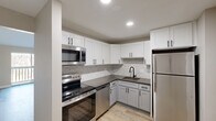Located at 560 Mill St, Unit C305 in Worcester, MA, this one-bedroom, one-bathroom residence offers a well-planned layout across a single floor. The kitchen is a standout feature, showcasing crisp white shaker cabinetry with matte black hardware, a decorative herringbone tile backsplash, dark granite-style countertops, and a full suite of stainless steel appliances including a range, over-the-range microwave, dishwasher, and refrigerator. Light wood-look flooring flows throughout the kitchen and living areas, lending a clean, contemporary feel. The living room is bright and airy, highlighted by vaulted ceilings, a sliding glass door that opens to a private balcony with tree-lined views, and a wall-mounted air conditioning unit supplemented by baseboard heating. A hallway connects the main living area to the private quarters. The bedroom offers plush carpeting, neutral walls, a built-in closet with bifold doors, and baseboard heating for year-round comfort. The bathroom is thoughtfully finished with wood-look flooring, a subway-tiled tub and shower surround, a vanity with a light stone-top, and matte black fixtures throughout, creating a cohesive, modern aesthetic.