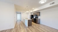 Located at 420–458 E 400 N in Vineyard, Utah, this single-floor residence offers a clean, contemporary design throughout. The open-concept kitchen serves as the heart of the unit, featuring dark wood cabinetry, granite-style countertops, a central island with a built-in sink, black appliances including a range and refrigerator, and stylish pendant lighting overhead. Light wood-style plank flooring runs through the main living areas and entryway, lending a warm and cohesive feel to the space. The living area leads to a private balcony accessible through a glass-paned door flanked by windows with horizontal blinds, offering scenic mountain views. The bedrooms are carpeted for added comfort and receive natural light through well-positioned windows, some of which also frame the surrounding mountain landscape. Two full bathrooms are finished consistently with dark wood vanities, granite-style countertops, large mirrors, and tub-shower combinations, all set on light wood-style flooring. The entryway provides a tidy transition into the unit with ample door storage options. Throughout, the space maintains a bright, neutral palette with white walls and clean lines, creating a modern and functional living environment.