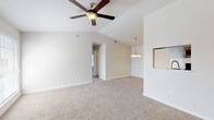Located at 1019 Friendship Lane in the heart of Fredericksburg, Texas, this single-story unit offers a thoughtfully designed layout with a clean, neutral aesthetic throughout. The open-concept living and dining area is highlighted by soaring vaulted ceilings and a ceiling fan, creating an airy and spacious feel. Plush wall-to-wall carpeting adds warmth underfoot, while large windows invite an abundance of natural light. A chandelier pendant fixture distinguishes the dining area, and a pass-through window connects it seamlessly to the kitchen.

The kitchen is well-appointed with stainless steel appliances, including a range, microwave, refrigerator, and dishwasher. Gray cabinetry pairs with light granite-style countertops, and wood-look flooring adds a touch of warmth to the space. A kitchen island with a sink provides additional prep and storage space.

The bedrooms are generously proportioned, each featuring soft carpeting and ceiling fans. Natural light filters in through sizable windows fitted with blinds. The bathroom is a standout space, showcasing bold, large-format dark tile surrounding a soaking tub, complemented by gray cabinetry with granite countertops and wood-look flooring, offering a stylish and functional finish.