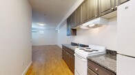 Located at 850 E Jones Ave in Phoenix, AZ, this single-floor unit offers a functional and efficient layout across a compact footprint. The open-plan kitchen and living area form the heart of the space, seamlessly connected to allow for flexible use. The kitchen is equipped with dark wood-toned cabinetry — both upper and lower — complemented by dark granite-style countertops, a built-in electric range, a refrigerator, a sink, and an under-cabinet range hood, providing ample storage and practical cooking functionality. The living area is bright and clean, featuring warm wood-look flooring that extends throughout the unit, crisp white walls, and windows with blinds that allow natural light to filter in. A wall-mounted ductless mini-split air conditioning unit ensures year-round comfort. The bathroom is finished with light ceramic tile flooring, a wall-mounted sink, a toilet, a mirror, and overhead lighting, maintaining a clean and utilitarian aesthetic. A sliding closet door is also visible in one area, offering additional storage. The overall ambiance is clean, minimal, and move-in ready, making it a straightforward and efficient space well-suited for everyday living in the Phoenix area.