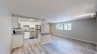 This single-floor unit offers a clean, contemporary design highlighted by light wood-style luxury vinyl plank flooring that runs consistently throughout the main living areas and bedrooms. The open-concept layout connects the kitchen directly to the living area, creating a spacious, connected feel ideal for everyday living and entertaining.

The kitchen is well-appointed with white shaker-style cabinetry, gray stone-finish countertops, and a full suite of stainless steel appliances including a refrigerator, electric range with over-the-range microwave, and dishwasher. A peninsula with a gray countertop serves as a natural divider between the kitchen and the living space. The living area benefits from natural light through multiple windows fitted with horizontal blinds, and a ceiling fan adds comfort to the room.

The bedroom features a ceiling fan, a closet with bifold doors, and a window overlooking the outdoors. The bathroom is finished with a white vanity, gray countertop, an undermount sink, and a mirrored medicine cabinet above, all set against neutral gray walls and light tile flooring.

A dedicated laundry area houses a stacked washer and dryer unit, offering convenient in-unit functionality. Textured ceilings and soft gray walls complete the cohesive, modern aesthetic throughout.