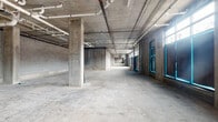 Located at 102 Washington Ave in Belleville, NJ, this ground-floor commercial shell space presents a substantial open-plan layout ready for customization. The space is constructed with concrete masonry unit (CMU) block walls and concrete structural columns throughout, lending an industrial character well-suited for a variety of commercial or creative uses.

The interior features polished concrete floors across the entire footprint, providing a clean and durable base. Overhead, an exposed concrete ceiling reveals a network of white utility piping, conduit runs, and fire suppression infrastructure, all of which remain visible and accessible. The layout is largely open and column-framed, allowing for flexible interior configurations.

Natural light enters through a series of large, floor-to-ceiling gridded windows and glass door assemblies along one elevation, brightening the space considerably and offering connectivity to the exterior. A utility panel and additional mechanical provisions are already in place, indicating readiness for tenant build-out.

The overall footprint is generous, configured in an elongated arrangement as seen in the schematic overview, with a secondary wing extending off the main volume. An access door is present within the space for interior circulation. This raw, unfinished shell presents a blank canvas ideal for retail, studio, event, fitness, or light commercial use in a growing New Jersey community.