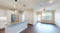 Located at 24500 Wildwood Park Rd in Richmond, TX, this well-appointed one-bedroom, one-bathroom residence offers a thoughtfully designed single-floor layout. The open-concept kitchen and living area serves as the heart of the home, showcasing rich dark hardwood-style flooring, crisp white shaker cabinetry, granite countertops, a center island with a sink, and stainless steel appliances including a refrigerator, range, and microwave. Pendant lighting above the island adds a modern touch, while recessed ceiling lights brighten the space throughout. The living area features large windows fitted with blinds that invite abundant natural light, along with a ceiling fan and a glass door that opens onto a private balcony overlooking lush green grounds and mature trees — a serene outdoor retreat. The bedroom is generously proportioned, finished with plush carpeting, a ceiling fan, and a window framing leafy views. It connects directly to a spacious walk-in closet outfitted with multiple hanging rods and shelving. The full bathroom is well-equipped with a granite-topped vanity, white cabinetry, a framed mirror, wood-style flooring, and a soaking tub with shower combination. Clean neutral tones and consistent finishes throughout create a cohesive, modern aesthetic.