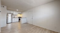 This single-floor unit presents a bright and functional layout designed for comfortable everyday living. The open-concept kitchen serves as a central feature, outfitted with crisp white cabinetry, granite-style countertops, stainless steel appliances including a refrigerator and gas range, a built-in sink, and a peninsula that extends the workspace while defining the transition to the living area. Light wood-look flooring flows throughout the main living space and kitchen, lending warmth and continuity to the interior. The textured ceiling adds a classic touch seen consistently throughout the unit. The bedrooms offer a cozy contrast with soft carpeted flooring and windows fitted with blinds that allow for natural light while maintaining privacy. One bedroom includes a ceiling fan and closet access, while another features a window-mounted air conditioning unit. The bedroom areas connect conveniently back toward the kitchen, creating an efficient and cohesive floor plan. Throughout the unit, neutral white walls provide a clean, versatile backdrop, and ample electrical outlets are positioned throughout each room. Overall, the space presents a tidy, move-in-ready feel with practical amenities suited for functional daily living.