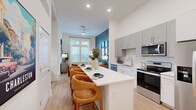 Located at 4939 Ohear Ave in North Charleston, SC, this thoughtfully designed 2-bedroom, 1-bathroom residence offers a cohesive blend of modern finishes and vibrant interior design across a single floor. The open-concept kitchen and living area serves as the heart of the home, featuring gray and white shaker cabinetry, subway tile backsplash, stainless steel appliances, and a white quartz island with bar seating — ideal for casual dining and entertaining. Light wood-style flooring flows throughout, enhancing the bright, airy atmosphere created by recessed lighting and a ceiling fan overhead. The living room makes a bold statement with a deep teal accent wall adorned with a curated gallery of framed artwork, complemented by large windows that invite natural light. The primary bedroom offers a serene retreat with a rich navy accent wall, tall windows with elevated transom panels, and a dedicated closet. The second bedroom mirrors the home's colorful character with its own striking two-tone accent wall. The full bathroom features a glass-enclosed shower, white vanity cabinetry, and a vivid red accent wall for a dramatic touch. Throughout the residence, high ceilings and a cohesive modern-eclectic aesthetic create an inviting and visually dynamic living environment.