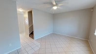 This two-story space offers a practical and functional layout with a clean, neutral aesthetic carried throughout. The main living area is generously sized, featuring light-toned ceramic tile flooring laid in a diagonal pattern, soft gray walls, and a textured ceiling fitted with a ceiling fan and light fixture. A staircase with carpeted treads connects the two levels, accessible directly from the living area. Large windows allow natural light to fill the entry-level rooms, contributing to a bright and open atmosphere.

The kitchen is designed with a pass-through bar that opens toward the living space, enhancing the sense of connectivity between rooms. Light wood cabinetry provides ample storage, complemented by light-colored countertops, a double-basin stainless steel sink, and a coil-burner electric range. The tile flooring continues seamlessly from the living area into the kitchen.

The bathrooms are finished with tile flooring and include light wood vanity cabinetry with white countertops and chrome fixtures. One bathroom features a full-sized soaking tub with a built-in grab bar and surround walls. A half bath with a single vanity, mirror, and toilet provides additional convenience. Throughout the space, consistent finishes and neutral color palettes create a cohesive and move-in-ready environment.