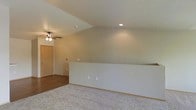 This single-floor residence offers a thoughtfully designed open layout that maximizes the sense of space and flow. A defining architectural feature is the vaulted ceiling, which adds volume and a feeling of openness to the main living area. Recessed lighting is installed in the ceiling, providing clean, even illumination throughout the space, while a ceiling fan offers both additional light and air circulation for year-round comfort.

The interior showcases a combination of two distinct flooring materials — warm hardwood flooring is present in one section of the space, lending a classic, durable aesthetic, while plush carpeting covers another area, adding softness underfoot and a cozy feel. A low half-wall divides these two zones, subtly delineating different areas of the floor plan while maintaining an open and connected atmosphere.

The neutral, warm-toned walls provide a versatile backdrop suitable for a variety of interior styles. Multiple electrical outlets are conveniently positioned along the walls, and a closet with sliding doors adds practical storage. The overall ambiance is clean, bright, and functional, making the space well-suited for comfortable everyday living.
