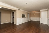 Located at 4999 Windsor Downs Lane in Decatur, Georgia, this single-story residence showcases a thoughtfully designed interior with consistent dark hardwood flooring throughout. The open-concept living and dining area is a standout feature, highlighted by classic white wainscoting panels, crown molding, and warm neutral-toned walls that create a polished, cohesive aesthetic. Natural light filters in through multiple windows fitted with blinds, lending brightness to the generous living spaces.

A pass-through opening connects the living area directly to the galley-style kitchen, which is well-appointed with sage-green cabinetry, granite-look countertops, black appliances including a range and refrigerator, and a double sink positioned beneath a window. Ample upper and lower cabinetry provides substantial storage throughout the kitchen.

The bedroom offers a comfortable, spacious layout with a large walk-in closet and access to additional storage. The bathroom features a full tub-shower combination with white tile surround and hardwood-style flooring. Throughout the unit, textured ceilings and clean white trim complement the warm wall tones, contributing to an inviting and well-maintained overall ambiance.