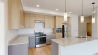 This well-designed 2-bedroom, 2-bathroom residence offers a clean, contemporary aesthetic throughout its single-level floor plan. Light hardwood flooring flows seamlessly across the main living areas, complementing the bright, white walls and recessed lighting that give the space an open, airy feel.

The kitchen is a standout feature, equipped with stainless steel appliances including a gas range, built-in microwave, and refrigerator. Light wood cabinetry extends to the ceiling for ample storage, while gray lower cabinets and granite-style countertops add a modern contrast. A peninsula with pendant lighting and an integrated sink serves as both a functional workspace and a casual gathering point, opening directly into the living area.

The primary bedroom is generously sized, featuring large windows that fill the room with natural light and views of the surrounding urban streetscape. A ceiling fan adds comfort and practicality. The second bedroom mirrors this bright, clean design with dual tall windows and hardwood floors.

Both bathrooms are finished with tile flooring and light wood vanities topped with granite countertops. The primary bath includes a full soaking tub and shower combination, while the second bath offers a walk-in shower configuration. A dedicated closet provides additional storage. Throughout the residence, the design prioritizes clean lines, natural light, and a cohesive, modern palette.