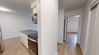 Located at 535–555 Shaw Ave in Coquitlam, BC, this 1-bedroom, 1-bathroom unit offers a thoughtfully designed layout across a single floor. Light wood-tone laminate flooring runs throughout, creating a warm and cohesive aesthetic in every room.

The open living area is bright and airy, anchored by a large sliding glass door that opens to a private balcony overlooking lush, mature greenery — a serene natural backdrop that brings the outdoors in. The space is finished with clean white walls and a textured ceiling.

The kitchen is well-equipped and efficient, featuring white shaker-style cabinetry, dark countertops, subway tile backsplash, stainless steel appliances including a refrigerator, electric range, and over-the-range microwave, plus a stainless steel sink. A breakfast bar provides additional counter space and casual seating.

The bedroom is a comfortable, quiet retreat with a window framing treetop views, light-toned flooring, and a dedicated closet for ample storage.

The bathroom is finished with clean white subway tile surrounding a full soaker tub and shower combination, complemented by chrome fixtures and a sliding glass door — a crisp, functional design.

Overall, this unit combines practical living spaces with modern, neutral finishes in a green, residential Coquitlam neighbourhood.