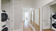 Located at 8601 Bergenline Avenue in North Bergen, NJ, this well-appointed two-bedroom, two-bathroom residence offers a thoughtfully designed single-floor layout with modern finishes throughout. Light hardwood flooring flows seamlessly across the space, complemented by crisp white walls that enhance the bright, airy atmosphere.

The open-concept kitchen and living area serves as the heart of the home. The kitchen features floor-to-ceiling white shaker cabinetry, a textured tile backsplash, stainless steel appliances, and a large central island with quartz countertops and bar seating — ideal for both cooking and entertaining. A stylish pendant light fixture adds a contemporary accent overhead.

The living room is bathed in natural light through expansive floor-to-ceiling windows, offering stunning panoramic views of the New York City skyline. Sliding glass doors open onto a private balcony, extending the living space outdoors.

Both bedrooms are generously sized, each benefiting from large windows that frame the NYC skyline. The primary bedroom provides ample closet space, while five closets throughout the unit offer exceptional storage. Both bathrooms are finished with marble-look tile, LED-backlit mirrors, and modern vanities. A dedicated laundry area and a welcoming hallway adorned with gold-framed mirrors complete this refined residence.