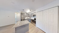 Located at 343C Fieldpointe Blvd in Frederick, Maryland, this single-floor residence offers a well-organized layout with a clean, contemporary aesthetic throughout. The open-concept kitchen and living area serves as the heart of the unit, featuring light hardwood-style flooring that extends across the main living spaces, creating a cohesive and airy feel. The kitchen is equipped with a full suite of stainless steel appliances, including a refrigerator, electric range, built-in microwave, and dishwasher. Grey shaker-style cabinetry provides ample storage, complemented by light quartz countertops and a peninsula island that adds both workspace and a natural division between the kitchen and living area. An elegant chandelier overhead adds a refined touch. The living room is bright and open, benefiting from a large sliding glass door dressed with vertical blinds that invites natural light and provides outdoor views. The bedrooms feature plush carpet flooring and windows overlooking the surrounding greenery and grounds, with at least one bedroom offering a walk-in closet with built-in shelving. The bathroom includes a grey vanity with a quartz-style countertop and light wood-style flooring, maintaining the unit's consistent, modern palette throughout.