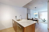 Located at 4845 Ch De La Côte-Saint-Luc in Montréal, this thoughtfully designed one-bedroom, one-bathroom unit offers a contemporary living experience defined by quality finishes and a cohesive modern aesthetic. The open-concept layout seamlessly connects the kitchen, dining, and living areas, maximizing the efficient use of space throughout the single floor.

The kitchen is a standout feature, centered around a striking island with a waterfall-edge quartz countertop accented by natural veining. Warm walnut cabinetry pairs with stainless steel appliances, including a built-in oven and dishwasher, while light hardwood flooring runs continuously into the living and dining areas. Exposed concrete ceiling panels add an industrial-chic character that carries through the entire unit.

The living room is bright and inviting, benefiting from large floor-to-ceiling windows dressed in sheer curtains that bathe the space in natural light. The bedroom features the same exposed concrete ceiling and accent wall, a generous closet, and a window offering ample natural light. The bathroom is finished with large-format light tile flooring, a walnut vanity with a white countertop, and a mirrored medicine cabinet, maintaining the unit's clean and modern design language throughout.