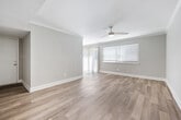 This single-floor, 2-bedroom, 2-bathroom unit offers a thoughtfully organized layout that balances open living areas with private bedroom spaces. The main living area features light-toned hardwood flooring, crisp white walls, and a vaulted ceiling detail that enhances the sense of openness. A ceiling fan adds functionality, while a window allows natural light to fill the space with a bright, airy feel.

The kitchen is equipped with light wood cabinetry, granite-look countertops, a stainless steel refrigerator, and a range, all accented by crown molding that carries throughout much of the unit.

The primary bedroom is generously sized, finished with plush carpet, crown molding, a ceiling fan with light fixture, and dual closets with bifold doors for ample storage. A dedicated walk-in style closet with built-in shelving provides additional organization. The second bedroom also features carpet, a ceiling fan, crown molding, and a window with blinds.

Both bathrooms include tub-shower combinations, wood-toned vanities with granite-look countertops, and light hardwood-style flooring. A hallway connects the bedrooms and bathrooms, completing the functional and cohesive floor plan.