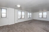 This single-floor residential unit offers a well-organized layout designed for comfortable everyday living. The main living area is generously proportioned, finished with wall-to-wall carpet and lined with multiple double-hung windows that allow abundant natural light and provide elevated views of the surrounding cityscape. White walls throughout contribute to a clean, bright ambiance across the entire space.

The kitchen is efficiently designed with white cabinetry, dark countertops, a double stainless steel sink, a white electric range, and a dishwasher. Wood-look flooring in the kitchen provides a practical contrast to the carpeted areas. A pass-through opening connects the kitchen to the adjacent living and bedroom areas, enhancing the sense of openness.

The bedroom is a comfortable, carpeted room featuring corner windows that bring in natural light and outdoor views. It includes a dedicated closet with a full-width hanging rod, offering convenient storage. An additional walk-in closet is also present, providing ample organizational space.

The bathroom is cleanly finished with vinyl flooring, a white vanity with under-sink storage, a large mirror, a tub-shower combination, and accessibility-oriented grab bars. The layout is straightforward and functional, making efficient use of the available space throughout the unit.