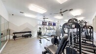 Located at 5050 Sam Houston Ave in Huntsville, Texas, this fitness center offers a generously sized, single-floor workout facility designed to support a full range of exercise routines. The space is finished with light wood-style flooring throughout, contributing to a clean and modern aesthetic that keeps the environment feeling open and inviting.

The cardio section is well-appointed, featuring multiple treadmills, elliptical trainers, a StairMaster step mill, and a stationary bike — all positioned along windows that let in ample natural light and offer views of the surrounding outdoor areas. Wall-mounted flat-screen televisions are distributed throughout the space, providing entertainment during workouts.

The strength training area includes a robust collection of cable machines, multi-functional weight stations, a dumbbell rack with a full range of free weights, and adjustable weight benches. Large floor-to-ceiling mirrors line portions of the walls, enhancing the sense of spaciousness and allowing users to monitor their form.

Ceiling fans with integrated lighting fixtures are evenly distributed across the white ceiling, ensuring proper air circulation and a bright, comfortable atmosphere. The interior walls feature subtle geometric accent designs and motivational framed artwork, adding personality to the space. The overall layout is thoughtfully organized, providing clear zones for both cardiovascular and resistance training activities.