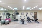 Located in Mountain View, California, this fitness and rehabilitation studio offers a clean, open, and professionally designed environment purpose-built for exercise and physical training. The single-floor space is laid out as one expansive open room, making efficient use of its footprint to accommodate a wide range of fitness activities.

The interior design emphasizes brightness and openness, with multiple skylights embedded in the white ceiling that flood the space with natural light. Recessed linear LED lighting complements the skylights, ensuring consistent, well-distributed illumination throughout. Light-toned hardwood-style flooring runs the length of the studio, contributing to an airy and inviting atmosphere.

A defining architectural feature is the extensive floor-to-ceiling glass mirror wall, which visually expands the space and supports movement-focused training by allowing users to monitor their form. The neutral, warm-white walls are accented with framed instructional and motivational artwork, adding a professional yet welcoming character.

The studio is outfitted with a thoughtful selection of fitness equipment, including resistance machines, rowing and sliding apparatus, a Pilates-style tower unit, stability balls, a ballet barre, and adjustable benches. Wooden cubby storage units and a blue exercise mat panel are neatly positioned along one wall. A private entrance door with a frosted glass panel provides a clean, professional transition point into the space.
