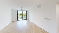 This well-appointed 2-bedroom, 3-bathroom residence offers a thoughtfully designed single-floor layout with a clean, contemporary aesthetic. Light wood flooring flows consistently throughout the space, complementing the crisp white walls and creating a bright, cohesive atmosphere.

The open-concept kitchen and living area serves as the heart of the home. The kitchen is equipped with stainless steel appliances, including a French door refrigerator, electric range, built-in microwave, and dishwasher. Cabinetry combines white upper cabinets with warm wood lower cabinets, accented by a distinctive geometric blue tile backsplash and light stone countertops. The adjoining living room features floor-to-ceiling sliding glass doors that flood the space with natural light and provide direct access to an outdoor balcony with lush tropical greenery views.

Both bedrooms are generously sized, each featuring ceiling fans, large windows or glass door access, and abundant natural light. The primary bedroom offers a comfortable footprint with outdoor views. A dedicated closet provides additional storage.

All three bathrooms are finished in a modern style, featuring wood-toned vanities, white countertops, backlit mirrors, glass-enclosed walk-in showers, and light wood flooring, maintaining the residence's consistent, contemporary design language throughout.
