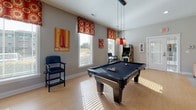 Located at 5825 Addison Park Drive in Huntsville, Alabama, this single-story community amenity space is designed to provide residents with a comfortable and engaging gathering environment. The space is organized into distinct functional zones, each thoughtfully furnished and decorated with a cohesive color palette of warm yellows, bold reds, and neutral grays throughout.

The lounge area features warm yellow accent walls and is furnished with a mix of red upholstered armchairs and colorful striped sofas arranged around a central area rug. A wall-mounted flat-screen television is positioned above a built-in cabinet, and a fireplace serves as a subtle focal point. Glass entry doors allow natural light to filter in, brightening the inviting atmosphere.

An adjacent game room offers light hardwood-style flooring, large windows with decorative patterned valances, and an abundance of natural light. This space is anchored by a full-size billiards table illuminated by pendant lighting, complemented by an arcade game cabinet and wall-mounted artwork.

A dedicated TV viewing nook provides a more intimate setting, with carpeted flooring, a wall-mounted screen, and comfortable seating arranged for relaxed viewing. The overall ambiance of the space is lively yet welcoming, designed to encourage social interaction and recreation.
