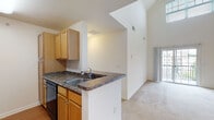 Located at 7102 Autumn Dr in Tinton Falls, NJ, this two-story residence offers a well-considered layout with bright, open living spaces across both levels. The living room is a standout area, showcasing dramatically vaulted ceilings that rise to impressive heights, a large sliding glass door opening to a private balcony, and a clerestory window that floods the space with abundant natural light. Plush wall-to-wall carpeting throughout the living and bedroom areas adds warmth and comfort underfoot. The galley-style kitchen is efficiently designed, featuring warm honey-toned cabinetry, dark granite-look countertops, a full suite of black appliances including a gas range, built-in microwave, refrigerator, and dishwasher, as well as a peninsula with a sink that overlooks the living area. The bedrooms are generously proportioned, each with soft carpeting, natural light from oversized windows with neighborhood views, and ceiling fans for added comfort. At least one bedroom benefits from a spacious walk-in closet with built-in shelving and rod storage. The bathroom is finished with neutral tile flooring, a single-sink vanity with wood cabinetry, and a tub-shower combination. The two-story floor plan, accentuated by a staircase with a classic wood banister, creates a distinctive sense of volume and openness throughout the home.