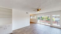 This single-floor residence offers a thoughtfully designed layout that balances comfort and functionality across its living, sleeping, and service areas. The main living space is bright and open, featuring durable wood-style plank flooring, crisp white walls, and a ceiling fan with light fixture overhead. A textured ceiling adds character throughout, while a sliding glass door floods the room with natural light and provides access to an outdoor balcony with pleasant views of surrounding greenery.

The kitchen is outfitted with warm wood-toned cabinetry on both the upper and lower levels, a mosaic tile backsplash in earthy and neutral tones, an electric cooktop, a built-in dishwasher, and an extended breakfast bar countertop that opens toward the living area—ideal for casual dining or entertaining.

The bedroom features soft carpeted flooring, a ceiling fan, a sliding closet, and a painted brick accent wall that adds texture and visual interest. Direct access to the bathroom is conveniently located nearby.

The bathroom is finished with a distinctive blue and white mosaic tile surround on the vanity countertop, a large mirror with built-in medicine cabinet, and wood-style flooring. Additional built-in linen storage is located just outside the bathroom, maximizing organizational space. Throughout the residence, the clean, neutral palette creates a cohesive and inviting atmosphere.