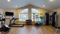Located at 20650 NE Halsey St in Fairview, Oregon, this well-equipped fitness center is housed in a single-floor facility designed to support a comprehensive range of workout routines. The space is defined by its striking vaulted ceilings with prominent arched windows that flood the main workout area with abundant natural light, creating an open and energizing environment. Warm-toned hardwood-style flooring runs throughout, adding a clean and inviting aesthetic to the space.

The main workout area is generously appointed with a treadmill, a full dumbbell rack with a wide range of weights, a cable resistance training machine, a medicine ball and resistance band rack, and an assortment of stability and exercise balls. This zone benefits most from the soaring ceiling height and the expansive arched window views to the outdoors.

An adjacent section of the facility houses additional strength equipment, including a multi-function cable machine, a weight bench, and a leg press/extension machine, with windows providing supplemental natural light. A separate dedicated cardio room features a stationary bike, an elliptical trainer, and a treadmill, accompanied by a wall-mounted television for entertainment during workouts.

Informational charts and sanitation stations are thoughtfully placed throughout the facility, supporting a safe and organized exercise environment.