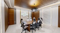 Located at 855 Main Street in Bridgeport, Connecticut, this professional conference room is a single, thoughtfully designed office space that exudes modern sophistication. The room is anchored by a substantial walnut conference table surrounded by ergonomic high-back mesh chairs, comfortably seating up to eight participants. A striking black multi-light ring chandelier serves as the focal point overhead, suspended beneath a warm wood-paneled ceiling accented with recessed linear lighting that casts an even, refined glow throughout the space. The walls feature a compelling contrast of richly grained wood paneling and floor-to-ceiling white Calacatta marble slabs, lending the room a high-end, executive aesthetic. The Soundview brand logo is prominently backlit in gold and white on the marble feature wall, reinforcing a strong professional identity. Large-format polished marble tile flooring extends the luxurious material palette underfoot. Glass partition walls on one side provide visual connectivity to the adjacent office area while maintaining acoustic separation. The cohesive blend of natural wood tones, marble surfaces, and carefully curated lighting creates a polished and focused environment well-suited for professional meetings and collaboration.