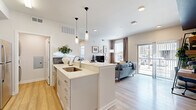 This efficiently designed single-floor residence offers a thoughtfully planned open-concept layout that maximizes its compact footprint. Light wood-tone flooring extends throughout the main living areas, complementing the bright, neutral color palette and recessed lighting overhead.

The kitchen serves as a central hub, anchored by a peninsula with white quartz countertops and dual pendant lights. White shaker cabinetry extends to the ceiling, paired with a subway tile backsplash and a full suite of stainless steel appliances. A stacked washer and dryer unit is conveniently integrated nearby.

The living room is filled with natural light from large windows and a sliding glass door that opens to a private balcony with outdoor views. The space features a distinctive accent detail with a navy ceiling trim, adding a modern design touch.

The bedroom offers a tranquil retreat with plush carpeting, large multi-pane windows with transom lights above, and a bold teal-and-white striped accent wall. A dedicated closet provides organized storage.

The bathroom features light wood flooring, grey cabinetry with a white countertop vanity, a framed mirror with bar lighting, and a full bathtub with shower.