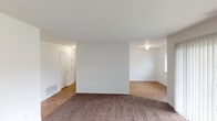 This single-floor unit in Indianapolis, IN, offers a straightforward and functional layout spread across several connected rooms. The living area is generously proportioned, featuring wall-to-wall brown carpet and crisp white walls that create a clean, neutral backdrop. A large sliding glass door fitted with vertical blinds allows natural light to fill the space and provides a view of the outdoors. An adjacent area with a window adds further brightness to the living space.

The kitchen is equipped with warm-toned wooden cabinetry offering ample upper and lower storage, granite-style countertops, a double stainless steel sink, and a white range. Wood-look flooring runs throughout the kitchen, and a closet near the entry provides additional storage. The space connects efficiently to the rest of the unit.

The bedrooms are carpeted and well-lit by windows fitted with horizontal blinds that overlook the surrounding area. Each room features white walls and clean lines, lending a simple, move-in-ready feel.

The bathroom includes a tiled tub-shower combination, a toilet, and a vanity with granite-style countertops, complemented by wood-look flooring and white tile wainscoting along the walls. Overall, the unit presents a practical and cohesive living environment.