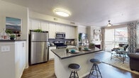 This two-story residence is thoughtfully designed with modern finishes and an open, functional layout. The kitchen serves as a central hub, showcasing white shaker-style cabinetry, a gray stone countertop, a tile backsplash, and a full suite of stainless steel appliances including a refrigerator, electric range, and over-the-range microwave. A peninsula with bar seating connects the kitchen seamlessly to the living area, which features wood-style flooring, crown molding, a fireplace, and large windows that invite natural light. The bedrooms are carpeted for comfort, with generous closet space and windows with blinds and curtain treatments. The primary bedroom is accompanied by an en-suite bathroom featuring a dual-sink vanity with gray countertops, white cabinetry, wood-style flooring, and a well-lit mirror. A secondary bathroom offers similar finishes with a single-sink vanity, a large mirror, and a shower-tub combination. A dedicated laundry room provides ample utility space with shelving and full-size washer and dryer hookups. Throughout the home, a neutral color palette, consistent flooring choices, and coordinated fixtures create a cohesive and inviting atmosphere across both floors.