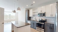 Located at 905 Lakeford Dr in Morrisville, NC, this thoughtfully designed single-floor residence offers 1 bedroom and 1 bathroom within a well-utilized, comfortable footprint. The open-concept kitchen and living area serves as the heart of the home, showcasing a striking herringbone-patterned tile backsplash, two-tone cabinetry in white and slate gray, stainless steel appliances, and a central island with a dark countertop accented by pendant lighting overhead. Light hardwood-style flooring flows seamlessly throughout the entire space, enhancing the bright, cohesive aesthetic. The spacious bedroom features multiple windows with tree-lined views, a ceiling fan, and access to two closets, providing ample storage. A hallway connects the bedroom to the full bathroom, which features white subway tile walls with contrasting dark trim. The unit also includes a dedicated laundry area for added convenience. Recessed lighting and large windows throughout ensure excellent natural light across all rooms. The neutral color palette, clean lines, and modern fixtures give the home a fresh, contemporary feel, making it a polished and functional residence in the Morrisville area.