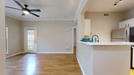 Located at 10809 Westwood Loop in San Antonio, TX, this 2-bedroom, 1-bathroom residence offers a practical and comfortable single-floor layout. Warm wood-look flooring runs throughout the space, lending a cohesive and inviting feel to every room.

The combined kitchen and living area forms the heart of the home. The kitchen is equipped with stainless steel appliances — including a refrigerator, electric range, and over-the-range microwave — alongside white cabinetry and light countertops that maximize the sense of brightness. A louvered pantry door adds a classic touch and functional storage.

The living room features neutral-toned walls, clean white baseboards, and a glass-paneled door that opens to a private balcony overlooking mature oak trees and the building's natural stone exterior — a charming outdoor retreat.

The primary bedroom is generously proportioned and filled with natural light from a large window, complemented by a ceiling fan with integrated lighting. The second bedroom also benefits from natural light and wood-look flooring. The bathroom is clean and straightforward, featuring a full tub-shower combination with white tile surround. Crown molding in the living and primary bedroom areas adds a refined architectural detail throughout.