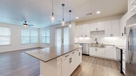 This single-floor residence offers a thoughtfully designed layout across two bedrooms and two bathrooms, with a clean, contemporary aesthetic carried consistently throughout. The open-concept kitchen and living area serves as the heart of the home, anchored by a substantial center island with a dark countertop and seating, illuminated by a trio of glass pendant lights. White shaker-style cabinetry lines the kitchen walls alongside a marble-look tile backsplash, stainless steel appliances, and a single-basin sink. The living area extends naturally from the kitchen, benefiting from multiple windows fitted with horizontal blinds that invite generous natural light.

Hardwood-style flooring runs throughout the main living areas, while soft carpet is found in both bedrooms and the walk-in closet. The primary bedroom is a comfortable size, featuring a ceiling fan and direct access to its en-suite bathroom, which includes a long white vanity with a quartz-style countertop, undermount sink, black-accented fixtures, and a framed mirror. The walk-in closet provides built-in shelving and double hanging rods for ample storage. The second bedroom also features a ceiling fan, carpeted flooring, and a well-sized window. Hallways are clean and bright, with white panel doors featuring black hardware completing the modern design language.