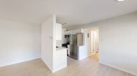 This well-maintained single-floor unit offers a clean, modern aesthetic throughout, characterized by bright white walls, light-toned luxury vinyl plank flooring in the main living areas, and an abundance of natural light. The open living and dining area is generously proportioned, featuring large windows and a front entry door that welcomes natural light and outdoor greenery views, creating an airy and welcoming atmosphere.

The kitchen is thoughtfully designed in a galley layout, showcasing white shaker cabinetry, light stone-finish countertops with a subtle tile backsplash, a stainless steel sink, and a full suite of stainless steel appliances including a refrigerator, gas range, and microwave. A pass-through peninsula connects the kitchen to the living space, enhancing the sense of openness.

The bedrooms are comfortably sized and finished with plush wall-to-wall carpeting, offering a softer, quieter feel. Each bedroom includes closet storage, with at least one featuring a dedicated reach-in closet with a hanging rod. Windows in the bedrooms allow for natural light while maintaining privacy.

The bathroom is finished in an all-white palette, complete with a tub-shower combination with tiled surround, a vanity with under-sink storage, and light wood-look flooring, contributing to a clean and functional design throughout the unit.