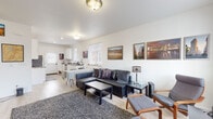 Located in Cheyenne, Wyoming, this single-story home offers a thoughtfully arranged layout with a clean, modern aesthetic throughout. The open-concept living and kitchen area forms the heart of the space, with light wood-tone flooring, white walls, and consistent natural light streaming through multiple windows with blinds.

The living area is generously proportioned, accommodating a large sectional sofa, coffee table, and a seating arrangement with lounge chairs and ottomans. Framed artwork decorates the walls, contributing a curated, welcoming character to the space.

The kitchen features white shaker-style cabinetry, dark granite-style countertops, and stainless steel appliances including a refrigerator, dishwasher, range, and microwave. A window above the sink and a door providing exterior access keep the kitchen bright and functional.

The bedroom is calm and simply appointed, with light flooring, white walls, and roller shades on the window. Ample storage is provided through a built-in dresser arrangement along one wall.

The bathroom is efficiently designed, incorporating a vanity with matching cabinetry and countertop, a shower/tub combination, and a stacked washer and dryer unit — consolidating laundry within the same space for added convenience.