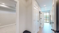Located at 350 Carraway Crossing in Chapel Hill, NC, this thoughtfully designed single-floor unit offers a cohesive blend of modern finishes and functional living spaces. The kitchen serves as a central highlight, featuring white shaker-style cabinetry that extends to the ceiling with glass-front upper cabinets and decorative X-detail accents. Stainless steel appliances — including a French door refrigerator, electric range, built-in microwave, and dishwasher — complement the clean white subway tile backsplash and light hardwood flooring throughout. A compact island provides additional counter and storage space. Floor-to-ceiling windows and sliding glass doors flood the kitchen and living area with abundant natural light while offering expansive views of the surrounding wooded landscape and balcony access. The bathroom is finished to a high standard, showcasing large-format marble-look tile in a spacious walk-in glass-enclosed shower with a built-in bench, paired with white cabinetry featuring matte black hardware and a dark countertop vanity. The bedroom is carpeted for comfort and includes access to a dedicated walk-in closet with built-in shelving and hanging rods. A skylight feature brightens an interior room, adding a distinctive architectural touch. The hallway connects all areas seamlessly, finished with crisp white panel doors and matte black hardware throughout.
