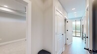 Located at 350 Carraway Crossing in Chapel Hill, NC, this thoughtfully designed single-floor unit offers a cohesive blend of modern finishes and functional living spaces. The kitchen serves as a central highlight, featuring white shaker-style cabinetry that extends to the ceiling with glass-front upper cabinets and decorative X-detail accents. Stainless steel appliances — including a French door refrigerator, electric range, built-in microwave, and dishwasher — complement the clean white subway tile backsplash and light hardwood flooring throughout. A compact island provides additional counter and storage space. Floor-to-ceiling windows and sliding glass doors flood the kitchen and living area with abundant natural light while offering expansive views of the surrounding wooded landscape and balcony access. The bathroom is finished to a high standard, showcasing large-format marble-look tile in a spacious walk-in glass-enclosed shower with a built-in bench, paired with white cabinetry featuring matte black hardware and a dark countertop vanity. The bedroom is carpeted for comfort and includes access to a dedicated walk-in closet with built-in shelving and hanging rods. A skylight feature brightens an interior room, adding a distinctive architectural touch. The hallway connects all areas seamlessly, finished with crisp white panel doors and matte black hardware throughout.