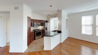 This thoughtfully designed single-floor residence offers a cohesive blend of modern finishes and functional living spaces. The open-concept kitchen is a standout feature, showcasing rich dark-stained cabinetry, dark granite countertops, a suite of stainless steel appliances including a gas range, microwave, and refrigerator, and a peninsula with a built-in sink that flows seamlessly into the living area. Warm hardwood flooring extends throughout the main living space, which is bright and airy, enhanced by multiple windows with blinds, crown molding, ceiling fans, and a glass-panel door leading to a private balcony. The balcony, framed by ornamental wrought-iron railings, offers picturesque views of lush trees, rolling hills, and the surrounding neighborhood. Bedrooms feature plush carpeting, ceiling fans, and natural light. The primary bathroom is well-appointed with a curved vanity, dark wood cabinetry, a large mirror, tile flooring, and a soaking tub with shower. A secondary bathroom offers a clean, tiled tub-shower combination. Additional highlights include a dedicated in-unit laundry area with a full-size washer and dryer, a generous walk-in closet with wire shelving, and ample storage throughout.