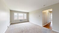 Located at 814 Ollie Ct in Carpentersville, Illinois, this single-floor unit offers a practical and well-organized layout across several distinct living spaces. Neutral, warm-toned walls and clean white trim are consistent throughout, creating a cohesive and understated aesthetic.

The spacious living area is covered in plush wall-to-wall carpet and features a large multi-pane window that draws in natural light while offering views of the surrounding neighborhood. A wall-mounted air conditioning unit and baseboard heating ensure year-round comfort. An open passage connects the living area to a hallway that leads to the remaining rooms.

A secondary carpeted room, also equipped with baseboard heating and a window with outdoor views, provides flexible use as a bedroom or additional living space. A separate entry area features a windowed exterior door and generous windows that flood the space with natural light.

The kitchen has been updated with gray shaker-style cabinetry, marble-look countertops, a matte black faucet and fixtures, and wood-look flooring. Black appliances, including a refrigerator, dishwasher, and range, complete the functional cooking space.

The bathroom includes a tub-shower combination with white tile surround, wood-look flooring, and chrome fixtures, maintaining the clean, neutral palette found throughout the unit.