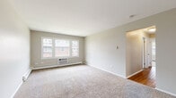 Located at 814 Ollie Ct in Carpentersville, Illinois, this single-floor unit offers a practical and well-organized layout across several distinct living spaces. Neutral, warm-toned walls and clean white trim are consistent throughout, creating a cohesive and understated aesthetic.

The spacious living area is covered in plush wall-to-wall carpet and features a large multi-pane window that draws in natural light while offering views of the surrounding neighborhood. A wall-mounted air conditioning unit and baseboard heating ensure year-round comfort. An open passage connects the living area to a hallway that leads to the remaining rooms.

A secondary carpeted room, also equipped with baseboard heating and a window with outdoor views, provides flexible use as a bedroom or additional living space. A separate entry area features a windowed exterior door and generous windows that flood the space with natural light.

The kitchen has been updated with gray shaker-style cabinetry, marble-look countertops, a matte black faucet and fixtures, and wood-look flooring. Black appliances, including a refrigerator, dishwasher, and range, complete the functional cooking space.

The bathroom includes a tub-shower combination with white tile surround, wood-look flooring, and chrome fixtures, maintaining the clean, neutral palette found throughout the unit.