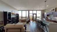 This single-floor residence offers a thoughtfully designed open-concept layout that seamlessly connects the main living spaces. The living room is anchored by floor-to-ceiling windows that flood the space with natural light and frame sweeping outdoor views, including what appears to be a waterfront skyline. Rich hardwood flooring runs throughout the main areas, complementing the modern aesthetic. A dedicated dining nook near the entry features warm wood tones and tall ceilings, adding an intimate yet airy feel.

The kitchen is a standout, outfitted with rich dark wood cabinetry, granite countertops, a mosaic tile backsplash, and a full suite of stainless steel appliances. A generous granite-topped island with bar seating serves as a natural gathering point between the kitchen and living area, enhanced by sleek pendant lighting.

The primary bedroom suite includes expansive built-in closet storage with floor-to-ceiling panel doors and direct access to a private balcony. Its en-suite bathroom features a glass-enclosed shower, granite vanity, and wood cabinetry. A secondary room functions as a flexible home office, complete with built-in closet space and tall ceilings. Throughout the residence, a neutral color palette and clean architectural lines create a cohesive, contemporary ambiance.