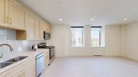 Located in the heart of downtown Oklahoma City, this 2-bedroom, 1-bathroom residence offers a well-designed layout filled with natural light and urban views. The open-concept living, dining, and kitchen area serves as the centerpiece of the home, where large windows with roller shades frame views of the surrounding cityscape and flood the space with daylight. The kitchen is outfitted with light wood cabinetry accented by gold hardware, a subway tile backsplash, stainless steel appliances including a range, microwave, and dishwasher, and a clean white countertop with an undermount sink. A bright, wide hallway connects the main living area to the private quarters, with recessed lighting overhead and neutral carpet underfoot throughout. The primary bedroom is generously sized, featuring dual windows with city views, a ceiling fan, and a double-door closet. The second bedroom also benefits from natural light via large windows and includes its own ceiling fan. The full bathroom showcases a light wood vanity with a dark stone countertop, gold fixtures, classic hex tile flooring, built-in shelving, and overhead cabinetry. A dedicated laundry area and four closets round out the practical features of this well-appointed downtown residence.