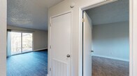 This single-floor residence offers a practical and comfortable layout across two bedrooms, two living areas, a kitchen, and a hallway. The kitchen is a standout feature, showcasing rich dark-stained wood cabinetry, light countertops, a tile backsplash, and a full suite of stainless steel appliances, including a range, dishwasher, and refrigerator. Warm wood-look flooring and a central overhead light fixture complete the space. The living areas are bright and open, featuring dark hardwood-style flooring, neutral walls, and sliding glass door access to an outdoor balcony, allowing natural light to fill the rooms. A textured ceiling runs throughout the common areas, lending a classic feel. The bedrooms are carpeted for warmth and comfort, each offering closet storage — including a sliding-door closet in the primary bedroom — and windows with outdoor views of surrounding trees and greenery. One bedroom also features a ceiling fan and additional natural light from a side-facing window. The hallway connects the spaces efficiently, with a built-in ventilation panel and access to the bathroom, which includes dark wood vanity cabinetry. Throughout, the space maintains a clean, neutral palette well-suited for a variety of living styles.