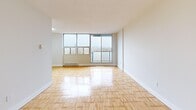 This 2-bedroom, 1-bathroom unit offers a practical and well-organized layout throughout its single floor. The bright living room is a standout feature, showcasing expansive floor-to-ceiling windows that frame panoramic city skyline views and allow abundant natural light to flood the space. Warm parquet flooring extends throughout the living room and both bedrooms, adding a classic character to the interiors. The primary bedroom is a comfortable size, offering a large sliding-door closet for ample storage and direct access to the hallway. The second bedroom also features parquet flooring and generous windows with outdoor views, complemented by a baseboard heating unit. The kitchen is finished with light tile flooring and includes built-in appliances, with cabinetry providing practical storage. The full bathroom is clean and simply appointed, featuring a full-sized soaking tub with an overhead shower, white subway tile surround, and chrome fixtures. A tiled hallway connects all rooms efficiently, with a utility panel mounted on the wall. The overall aesthetic is bright and neutral, with white walls throughout creating a clean, move-in-ready canvas.