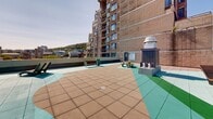 Located in the heart of Montréal's vibrant Plateau-Mont-Royal neighbourhood, this rooftop terrace at 350 Rue Prince-Arthur O offers an exceptional open-air experience with sweeping, unobstructed views of the city skyline and the iconic Mont-Royal to the north. The terrace is finished with a distinctive multi-toned tiled surface in shades of beige, mint green, and earthy tones, creating a visually dynamic outdoor environment.

The space is thoughtfully furnished to accommodate a variety of uses. Multiple wooden picnic-style tables with bench seating are positioned throughout, providing ample space for dining and social gatherings. Sleek lounge chairs are arranged to take full advantage of the sun exposure and panoramic sightlines. Tall planters filled with lush greenery and ornamental grasses add natural texture and a touch of landscape design to the urban setting.

Structural rooftop elements, including ventilation units and a mechanical access enclosure, are integrated discreetly into the layout. The terrace benefits from full open-sky exposure, making it an ideal space for enjoying Montréal's warm seasons. With its commanding views of the downtown core to the south and the green slopes of Mont-Royal to the north, this rooftop terrace serves as a distinctive and functional outdoor amenity.