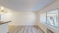 This efficient single-floor, one-bedroom, one-bathroom unit offers a thoughtfully arranged layout across five distinct spaces: a living room, bedroom, kitchen, bathroom, and hallway. Light wood-style laminate flooring runs consistently throughout, creating a cohesive and clean aesthetic. The living room features crisp white walls, a textured popcorn ceiling, and a window fitted with blinds that allows natural light to filter in, along with a wall-mounted HVAC unit for climate control. A doorway from the living room leads directly to the hallway and bathroom beyond. The galley-style kitchen is well-equipped with stainless steel appliances including a gas range, refrigerator, and microwave, complemented by white cabinetry, brown laminate countertops, and a double-basin stainless steel sink beneath a window. The bedroom is a comfortable, well-proportioned room featuring a ceiling fan with light fixture, a window with blinds providing natural light, and a full-width mirrored sliding closet that enhances the sense of space. The bathroom includes a tiled shower-tub combination with a window above, bringing in natural light. Overall, the unit presents a clean, neutral palette throughout.