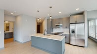 Located at 1331 Chester Ave in Raleigh's 27608 zip code, this modern single-floor residence showcases a clean, contemporary design with light wood-style flooring and a neutral gray color palette carried throughout. The open-concept kitchen serves as a true centerpiece, featuring a substantial island with a striking granite countertop, a matte black undermount sink, and stylish pendant lighting overhead. Sleek gray cabinetry with matte black hardware lines the walls, complemented by a white subway tile backsplash and a full suite of stainless steel appliances, including a range, microwave, and refrigerator with ice maker. The living area benefits from abundant natural light, courtesy of large windows fitted with horizontal blinds, and offers direct access to a private outdoor balcony. A ceiling fan adds comfort to the main living space. The unit includes two bathrooms: a full bath featuring a glass-enclosed walk-in shower with white tile surround and matte black fixtures, and a secondary bathroom appointed with a distinctive blue vanity, framed mirror, and stone-topped countertop. Additional rooms provide versatile, well-lit spaces with the same consistent flooring and clean wall finishes found throughout the residence.