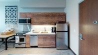 Located at 2615 S King St in Honolulu, Hawaii, this contemporary multi-bedroom unit offers a well-designed single-floor layout that maximizes both function and comfort. The kitchen is a standout feature, outfitted with rich walnut-toned cabinetry, stainless steel appliances including a range, dishwasher, microwave, and refrigerator, complemented by clean white countertops and under-cabinet lighting. The space accommodates multiple bedrooms, each with neutral tones, individual storage units, and windows fitted with horizontal blinds. Several bedrooms offer sweeping elevated views of the Honolulu cityscape and surrounding neighborhoods, filling the rooms with natural light. The living area features a wall-mounted air conditioning unit and a large window that frames panoramic city views, creating a bright and comfortable common space. Two bathrooms serve the unit, each with a shower, toilet, and vanity; one features a walk-in shower stall while the other includes a shower-tub combination. Polished concrete-style flooring runs throughout much of the unit, contributing to a modern, low-maintenance aesthetic. The overall design is clean, contemporary, and well-suited for shared living in the heart of urban Honolulu.